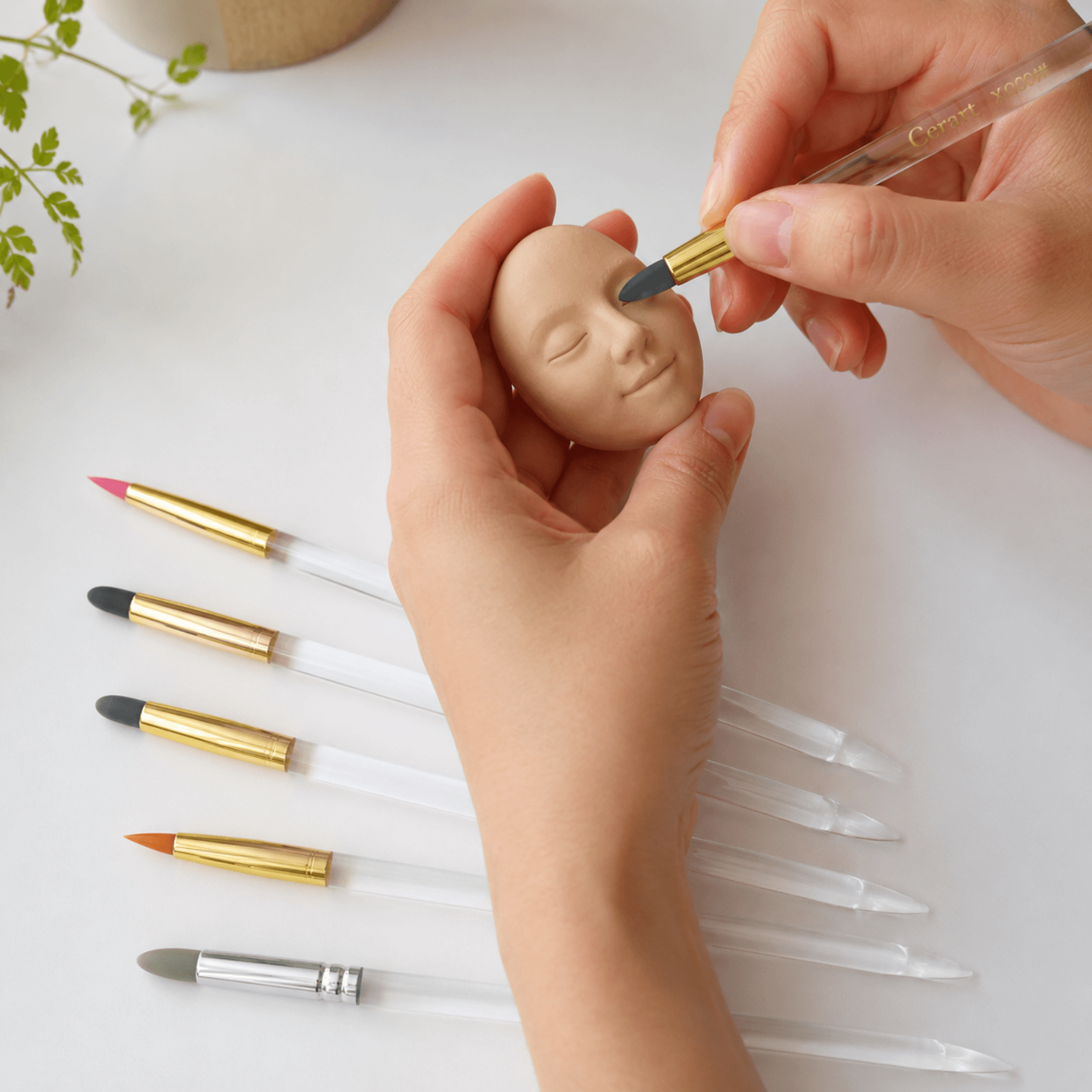 Manos modelando una carita con pinceles de silicona AradiaShop® sobre mesa de trabajo.